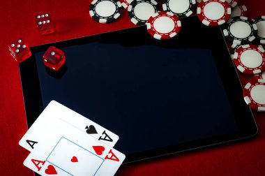 İnternet kumarhanesi ve online kumar konsepti dijital tablet üzerinde iki kart (as), zar oyunu oynamak için kullanılan zar, elektronik ped yüzeyinde siyah ve kırmızı poker çipleri ve kopyalama alanı