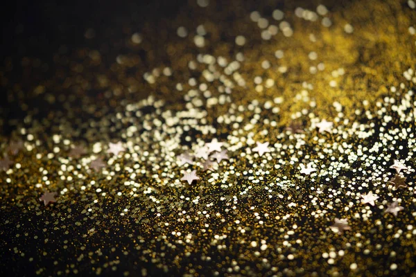 Beautiful Christmas light background. Abstract glitter bokeh and scattered sparkles in gold color, on black — Stock Photo, Image