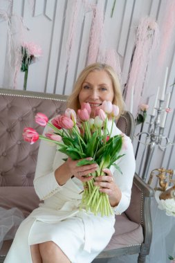 Zarif bir kadın şık, güzel dekore edilmiş bir yerde dururken canlı pembe laleler tutuyor.