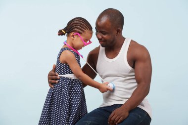 Mutlu baba ve doktor bir oyuncak stetoskop ile uçuk mavi arka plana karşı oynayan kız. O mavi puantiyeli elbise ve örgüler takıyor. Sleevless gömlek, kalın, o ona sevgiyle bakıyor.