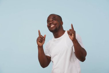 Beyaz T-shirt soluk mavi arka planı yapması yakışıklı kalın siyah adam. ararken, her iki elle de parmak işaret. Teşekkürler Tanrım jest. Memnun.