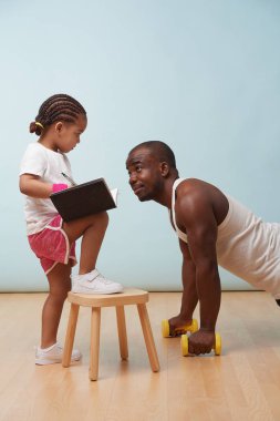 Sevimli küçük kızı fitness eğitim onu yakışıklı siyah genç babası. Kağıt defterine notlar alıyor. Çocuk rol oyunu. Onay için ona bakıyor. Ona sertçe bakıyor..