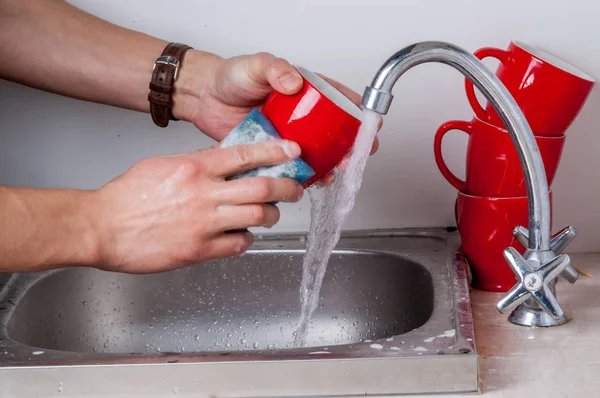 Mutfak lavaboda akan suyun altında sünger ile kırmızı Kupası erkek el yıkama. — Stok fotoğraf
