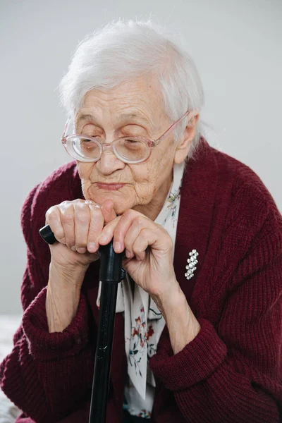 Portrait of a senior woman sitting on bed with walking stick at home — Stock Photo, Image