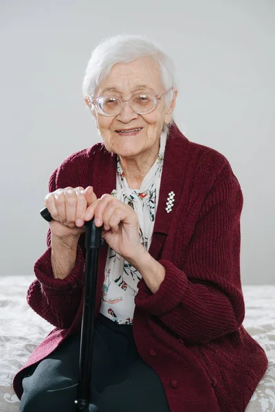 Cheerful senior woman sitting on bed with walking stick at home — Stock Photo, Image