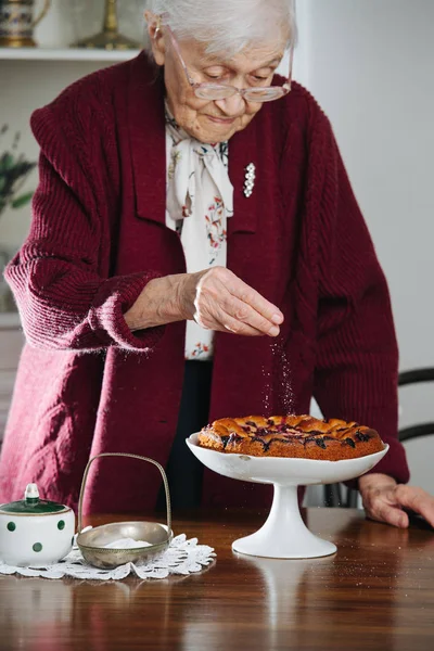 Senior woman pouring powdered sugar on tasty holiday pie on a table — Stock Photo, Image