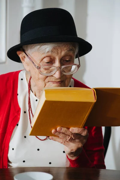 Kind grandmother is reading her book at dinner table at home. — Stock Photo, Image