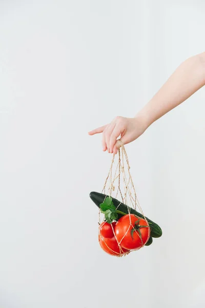 Hand holding little string bag with tomatoes and cucumbers