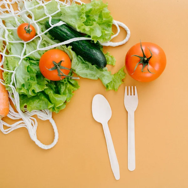 Spoon, fork and vegetables in a string bag — Stock Photo, Image