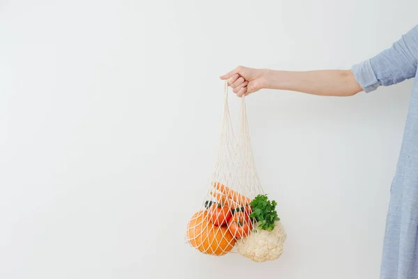 Hand holding string bag with vegetables
