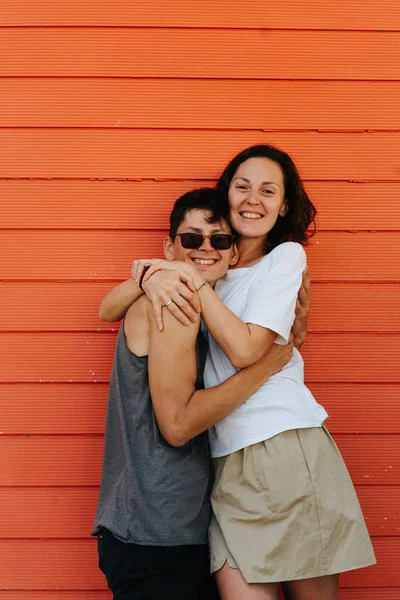 Feliz casal bonito compartilhando sua alegria contra a parede da casa laranja . — Fotografia de Stock