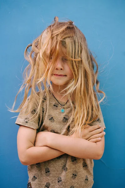 Little boy with long blond hair in white T-shirt posing in front of house wall. — Stock Photo, Image