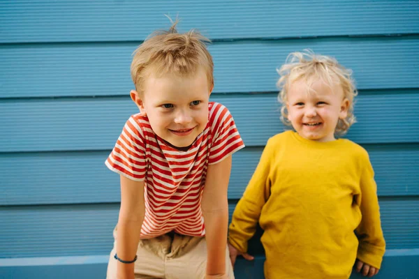 Outdoor portrait of big brother and his little sister against blue house wall — Stock Photo, Image