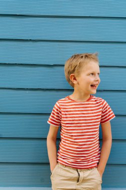 Mavi ev duvarının önünde poz çizgili t-shirt Sevimli küçük çocuk.