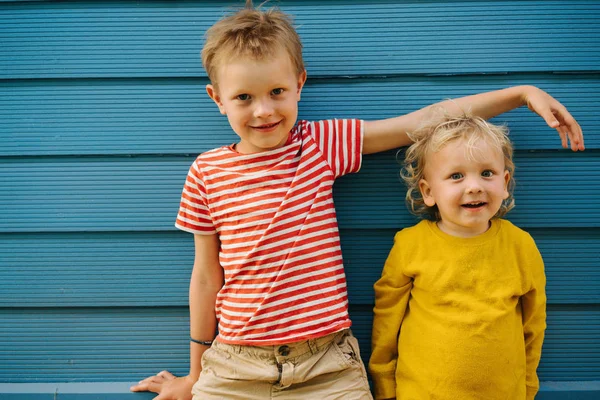 Außenporträt des großen Bruders und seiner kleinen Schwester vor blauer Hauswand — Stockfoto