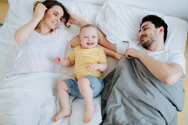 A fiatal család együtt pihen a szülők ágyában reggel. — Stock Fotó
