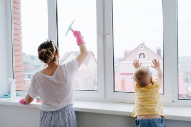 Bir bebek çocuk annesi temizleyici ile plastik pencere kapısı temizliyor