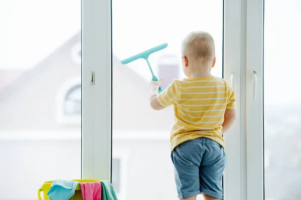 Funny little blond toddler boy is cleaning plastic window door with scrubber — Stock Photo, Image