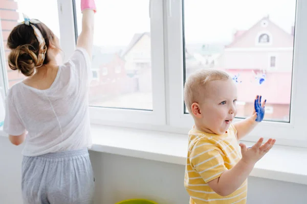 Mother of a toddler boy is cleaning plastic window door with wet cloth — Stock Photo, Image