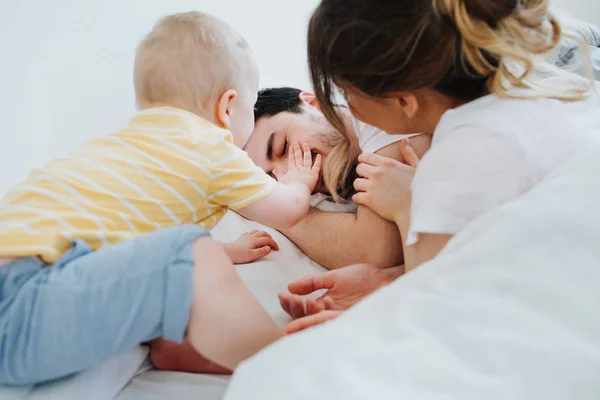 Cute little son along with his mother is trying to wake up his father — Stock Photo, Image