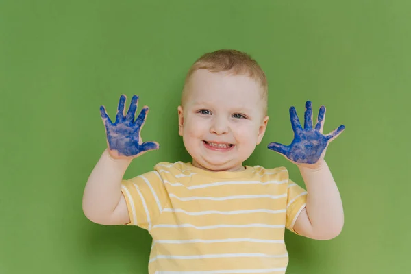 Портрет щасливого маленького хлопчика з синьою фарбою на руках на зеленому тлі — стокове фото