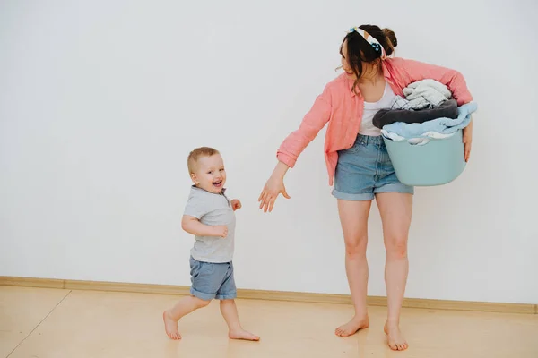 Young mother with laundry basin full of washed towels and her happy toddler son — Stock Photo, Image
