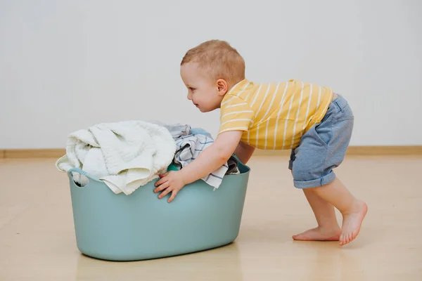 Little toddler boy is moving heavy laundry basin full of washed towels — Stock Photo, Image