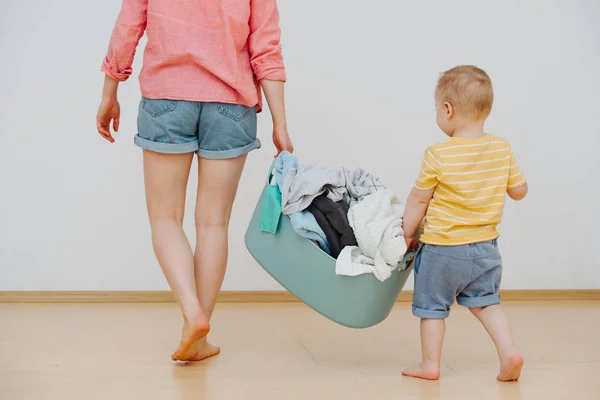 Joven madre y su feliz hijo pequeño con lavabo lleno de toallas lavadas —  Fotos de Stock