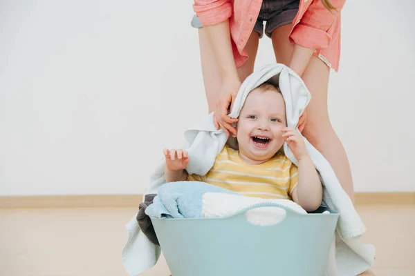 Happy toddler son sitting in laundry basin next to his mother — Stock Photo, Image