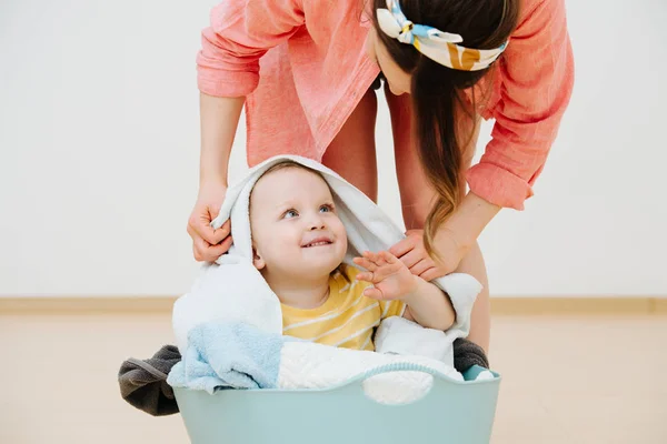 Happy toddler son sitting in laundry basin next to his mother — Stock Photo, Image