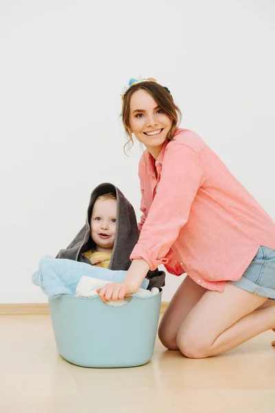 Happy toddler son sitting in laundry basin next to his mother