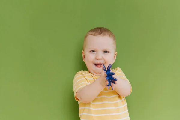 Portrait of happy little boy with blue paint on hands against green background — Stock Photo, Image