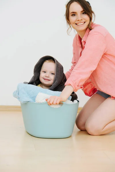 Happy toddler son sitting in laundry basin next to his mother — Stock Photo, Image