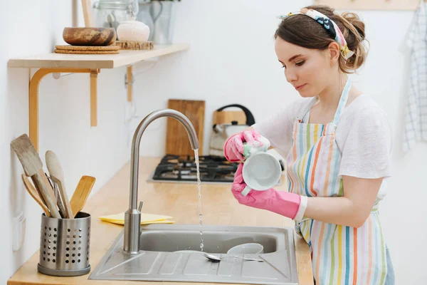 Joven mujer feliz en una cocina está lavando tazas y platos —  Fotos de Stock