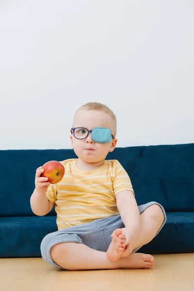 Pequeño niño en parche de ojo perezoso con una manzana en la mano — Foto de Stock