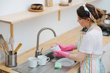 Mutfaktaki genç esmer kadın bardak ve bulaşık yıkıyor.