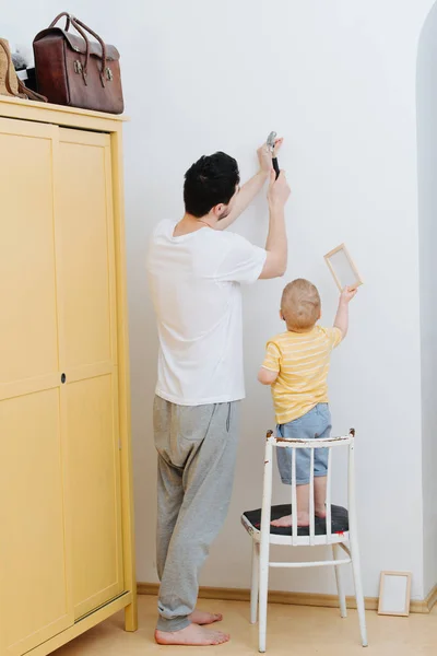 작은 유아 아들을 가진 아버지는 벽에 액자 그림을 부착하고 있습니다. — 스톡 사진