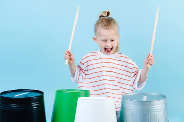 Little jolly boy using drumsticks on iron and plastic buckets. Playing rhythm.