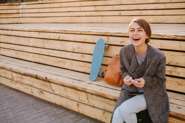 Jovem mulher rindo com um skate está sentado em um banco de 2 estágios . — Fotografia de Stock