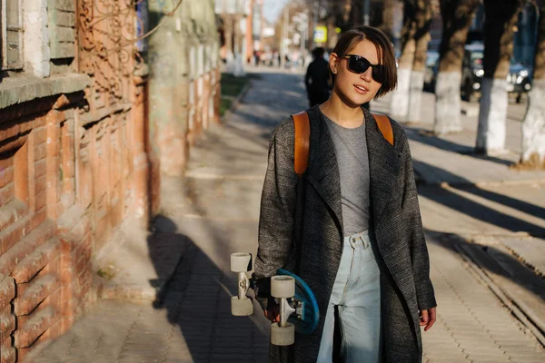 若い女性はスケートボードを持って通りを歩いている。ライフスタイル写真. — ストック写真