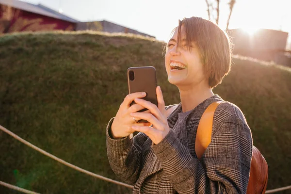 Jong gelukkig aantrekkelijk kortharig brunette vrouw met telefoon in een park — Stockfoto