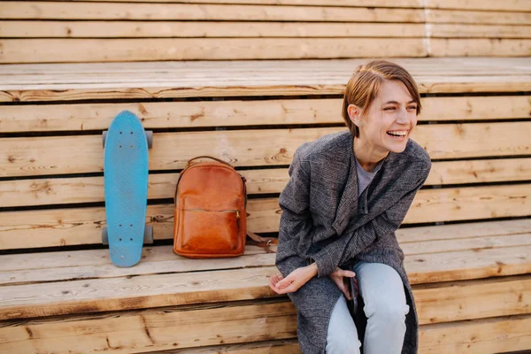 Молодая смеющаяся женщина со скейтбордом сидит на 2-х ступенчатой скамейке . — стоковое фото