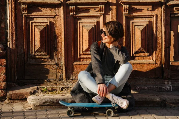 Belle jeune patineuse souriante assise dans un environnement urbain . — Photo