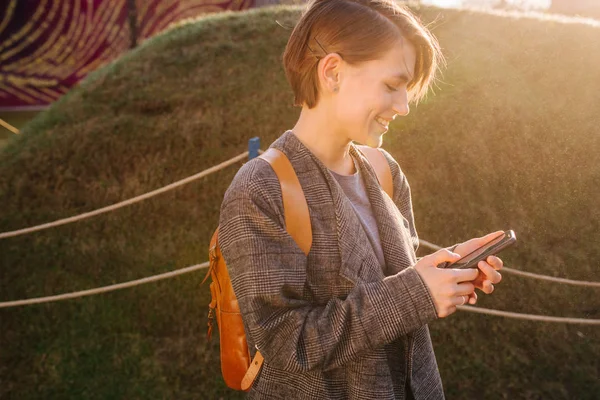 Ung, lykkelig, korthåret brunette kvinne med telefon i en park – stockfoto