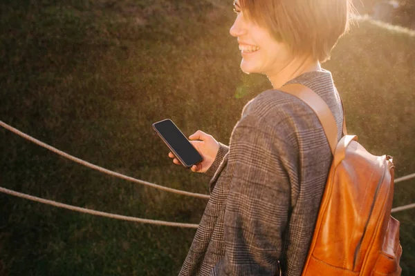 Ung, lykkelig, korthåret brunette kvinne med telefon i en park – stockfoto