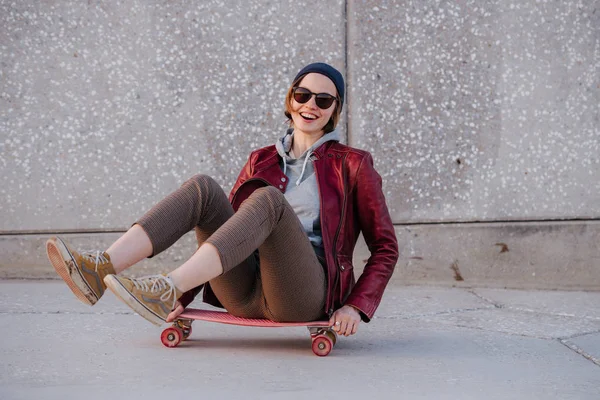 Jovem feliz luz morena mulher sentada em um skate em uma cidade — Fotografia de Stock