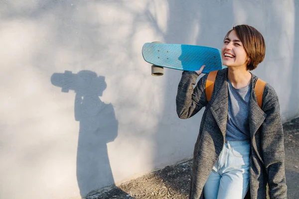 Jong gelukkig kortharig brunette vrouw met skate in handen in voor een muur — Stockfoto