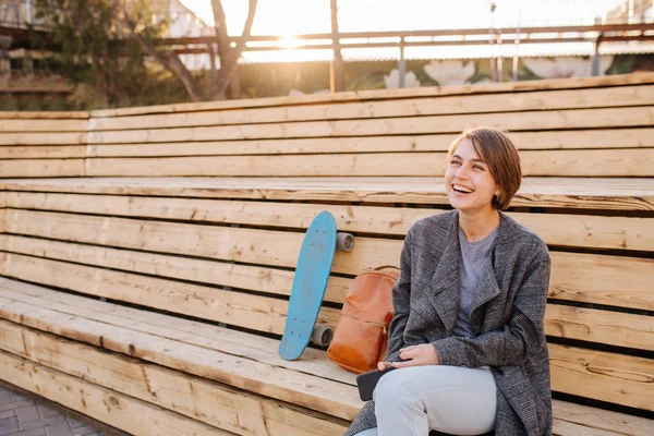 Jonge lachende vrouw met een skateboard zit op een 2-stage bank. — Stockfoto