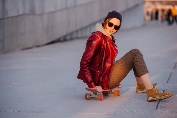 Giovane donna bruna felice luce seduta sul suo skateboard in una città — Foto Stock