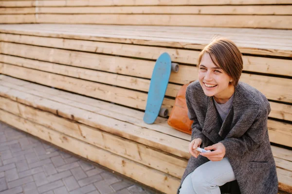 Joven mujer riendo con un monopatín está sentado en un banco de 2 etapas . — Foto de Stock